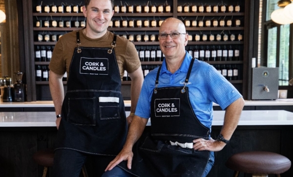 two people in cork and candles apron in front of wall of candles