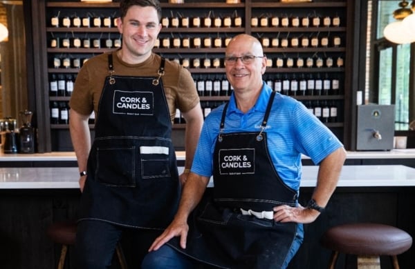 two people in cork and candles apron in front of wall of candles