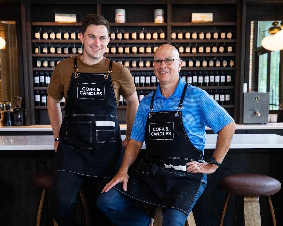 two people in cork and candles apron in front of wall of candles