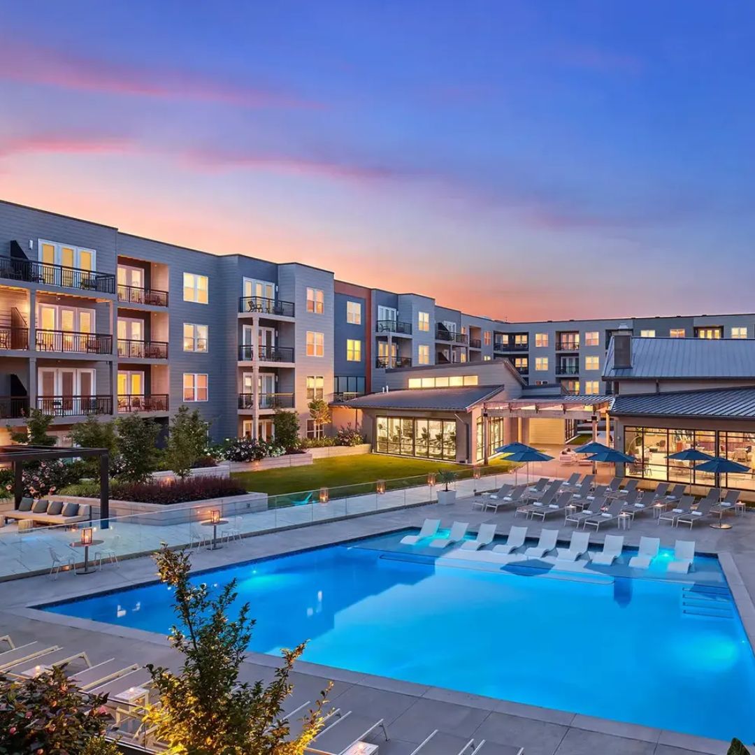 outdoor view of a large pool surrounded by an apartment building at sunset