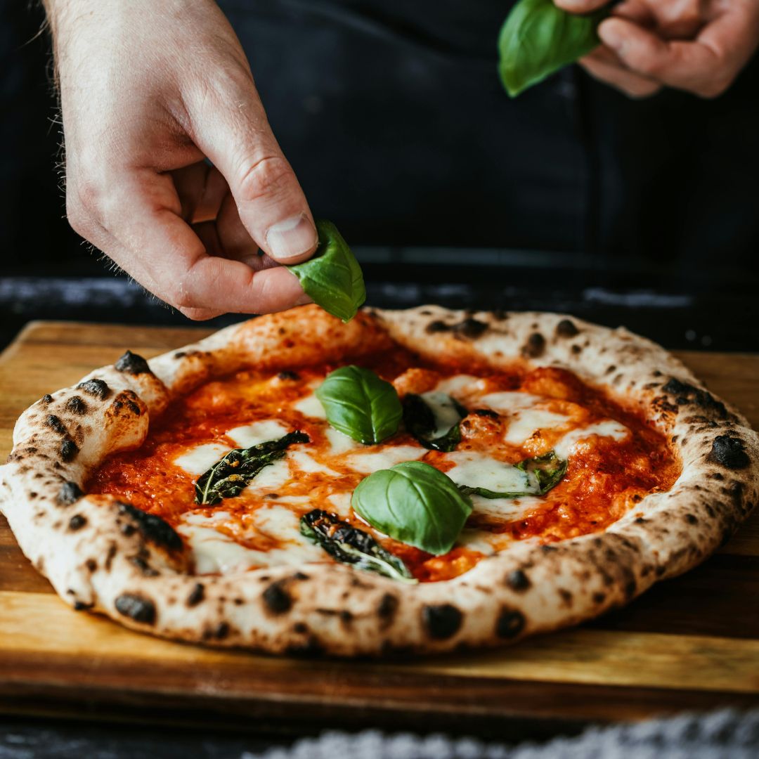 hand putting basil on a small pizza