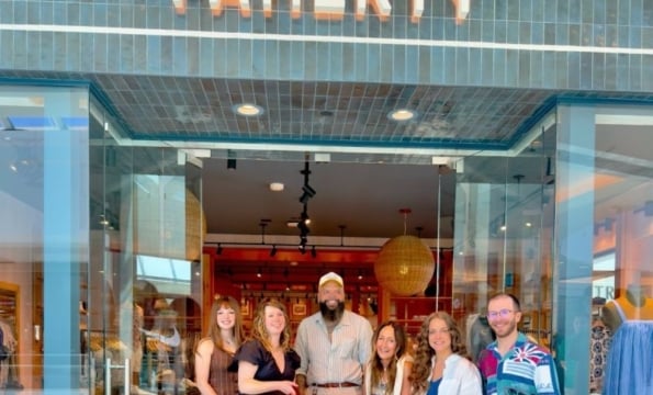 group of 6 people smiling behind a large red ribbon in front of a Faherty storefront