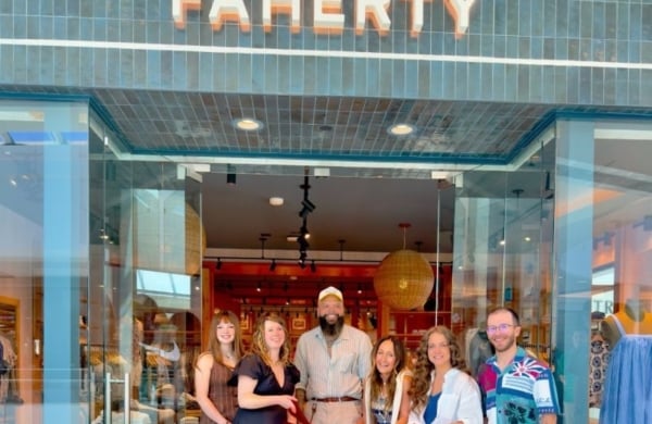 group of 6 people smiling behind a large red ribbon in front of a Faherty storefront