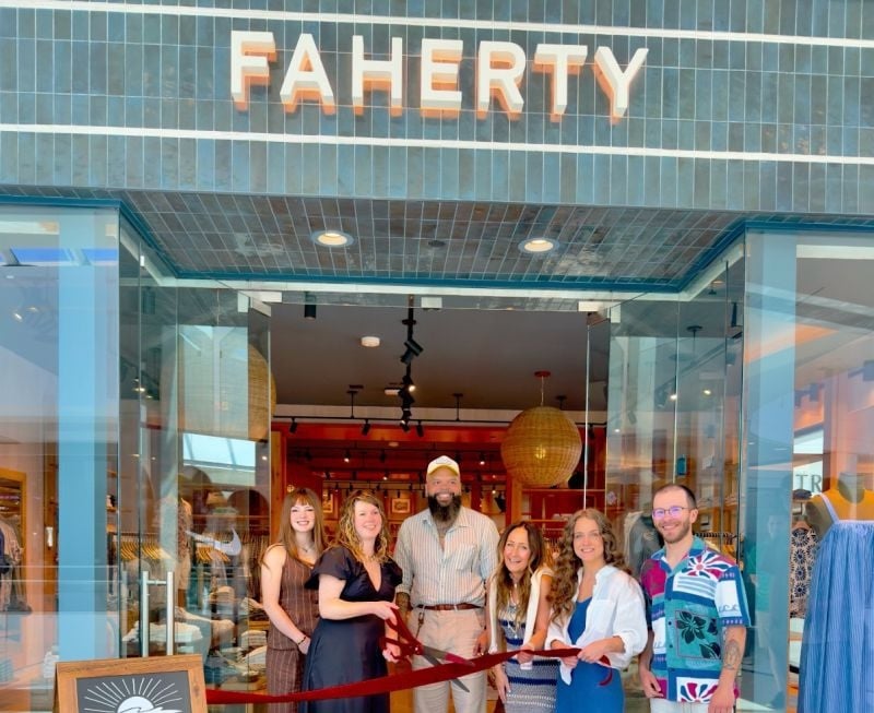 group of 6 people smiling behind a large red ribbon in front of a Faherty storefront