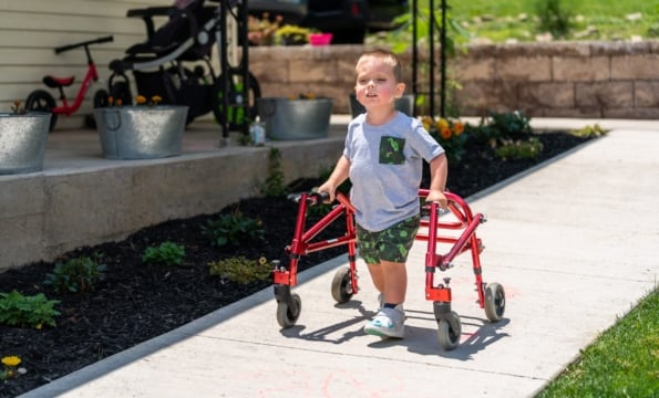 child using a red walking device down an outdoor sidewalk