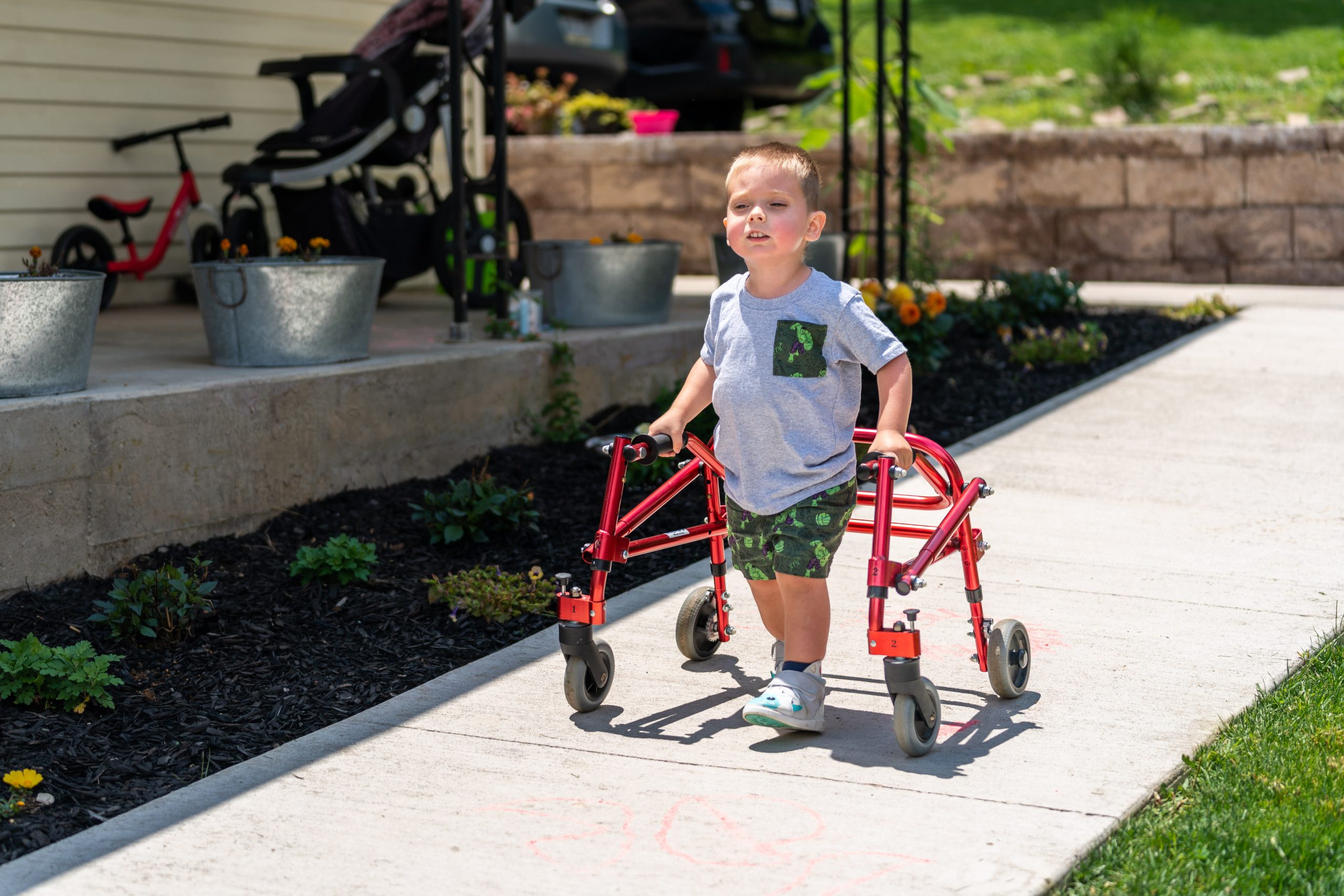 child using a red walking device down an outdoor sidewalk